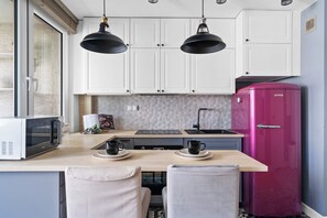A compact kitchen with white cabinets, a pink refrigerator, a microwave, and two pendant lights. - Solec Apartment (Warszawa)