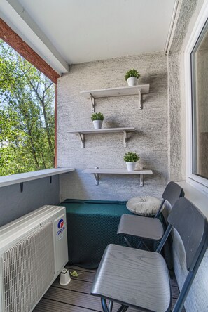 A balcony with a white radiator, a green cushioned bench, and three white shelves with potted plants. - Solec Apartment (Warszawa)