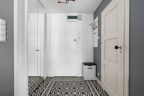 A hallway with a patterned floor, a white door, a small trash bin, and a thermostat on the wall. - Solec Apartment (Warszawa)