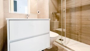 A modern bathroom with a glass shower enclosure, a white vanity, and a toilet. - Modern Home in Vicálvaro (Madrid)