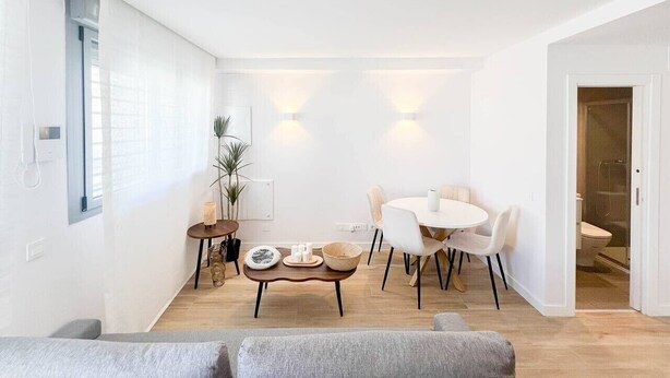 A modern living room with a dining area, a sofa, a coffee table, and a small side table with decorative items. - Modern Home in Vicálvaro (Madrid)