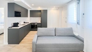 A modern kitchen with a built-in microwave, a grey sofa, and a small dining area. - Modern Home in Vicálvaro (Madrid)