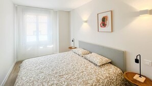 A bedroom with a bed, a bedside table, a lamp, and a window with curtains.