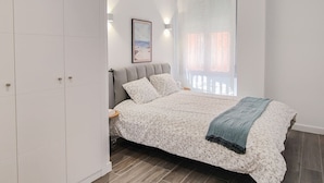 A bedroom with a bed, nightstands, a wardrobe, and a window with curtains. - Modern Home in Vicálvaro (Madrid)