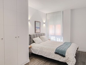 Een slaapkamer met een bed, nachtkastjes, een kledingkast en een raam met gordijnen.