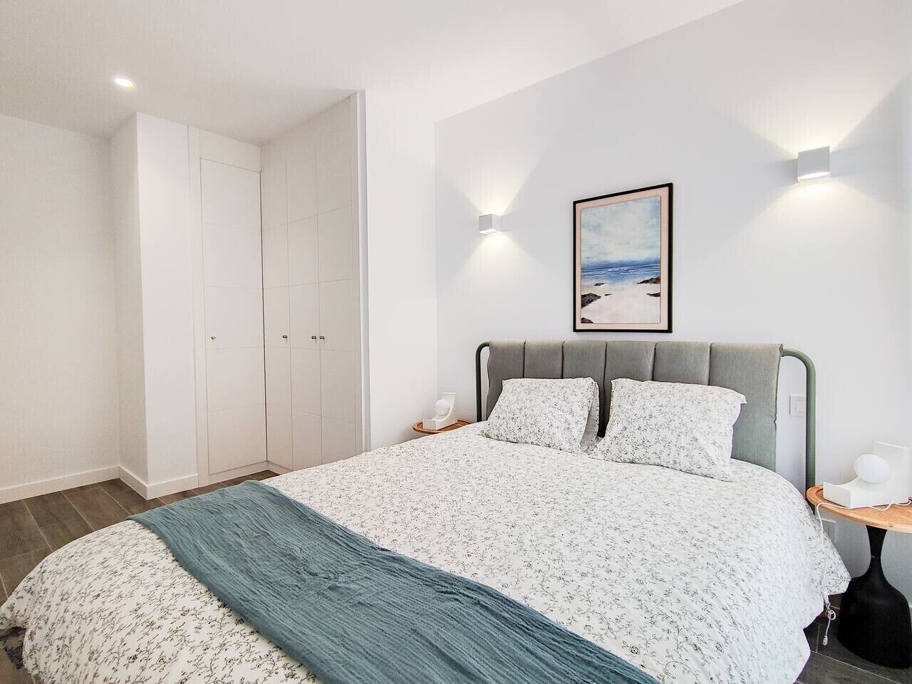 Een slaapkamer met een bed, een kledingkast, een nachtkastje en een aan de muur hangend schilderij.