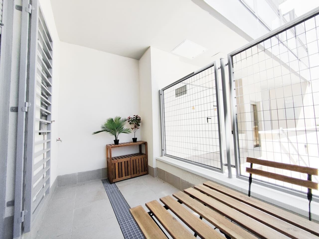 Un pasillo con un banco de madera, un pequeño estante de madera con plantas y una reja de metal.