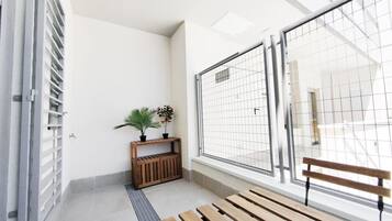 Un pasillo con un banco de madera, un pequeño estante de madera con plantas y una reja de metal.