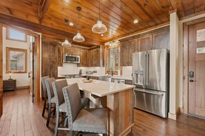 A kitchen with wooden cabinets, stainless steel appliances, and a central island with seating. - Peak a View  - Lux Cabin w Tri-State VIEWS at 4,200 Feet! (Beech Mountain)