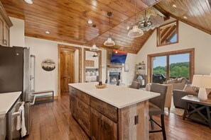 A spacious kitchen with a large island, wooden cabinets, and a stone fireplace. - Peak a View  - Lux Cabin w Tri-State VIEWS at 4,200 Feet! (Beech Mountain)