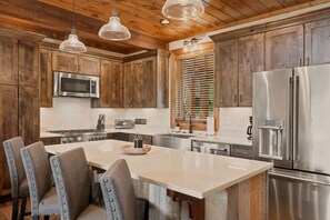 A modern kitchen with wooden cabinets, stainless steel appliances, and a central island with seating. - Peak a View  - Lux Cabin w Tri-State VIEWS at 4,200 Feet! (Beech Mountain)