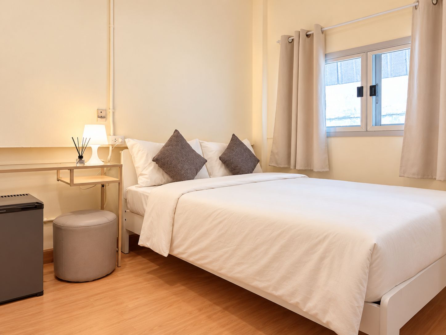 A hotel room with a bed, bedside table, lamp, and a small trash bin.
