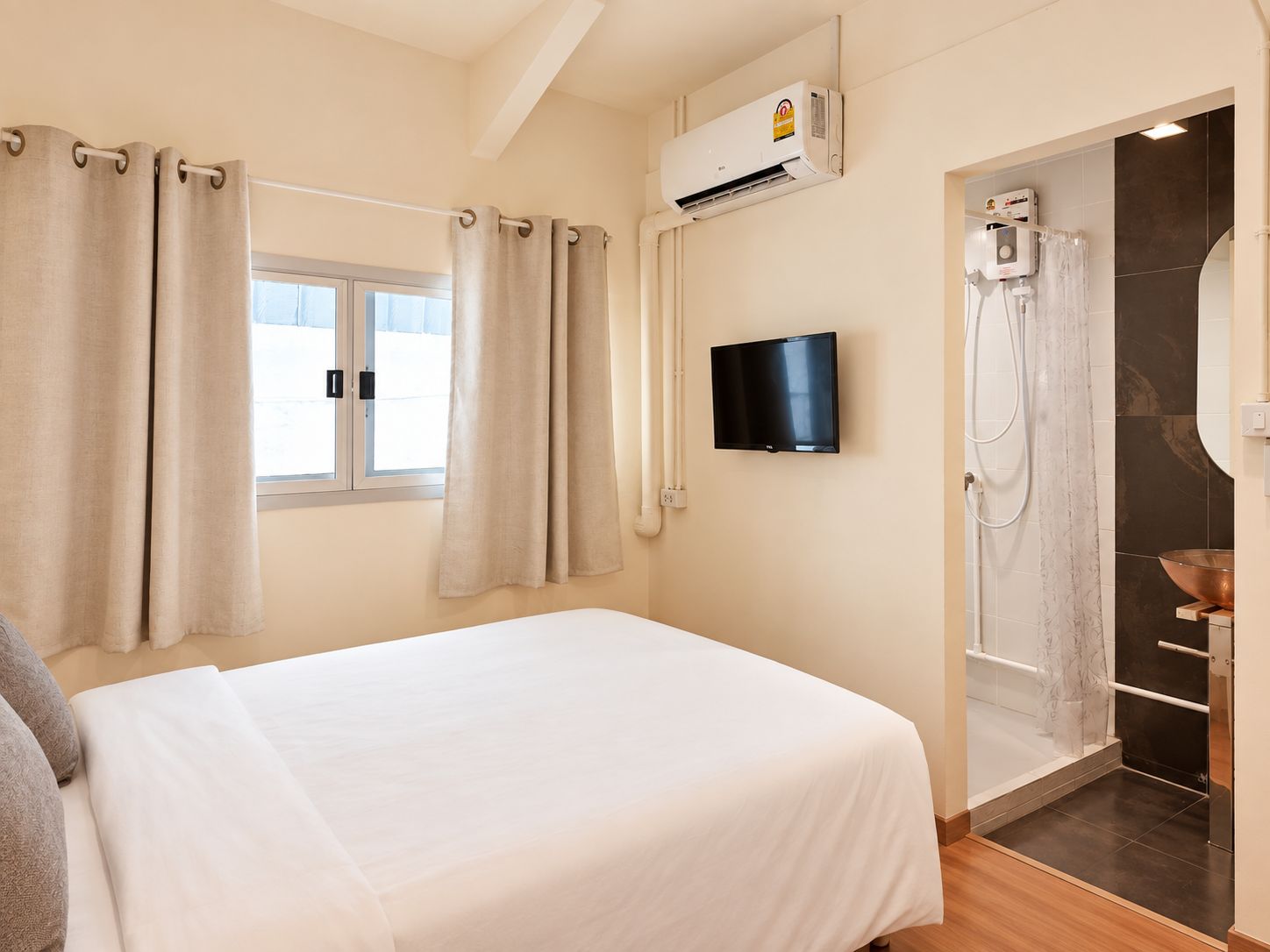 Habitación de hotel con cama, televisión, aire acondicionado, ducha y ventana con cortinas.