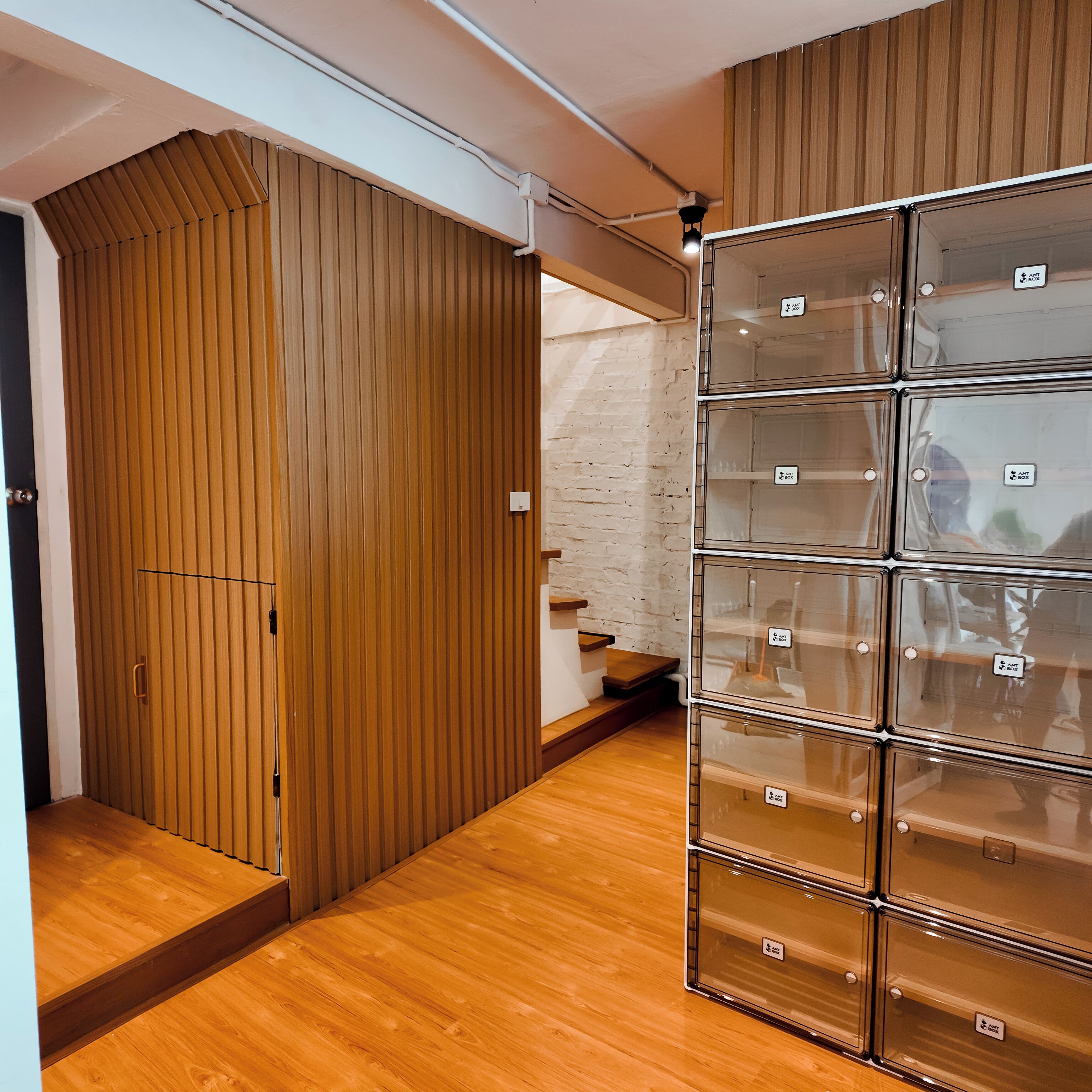 A room with a wooden wardrobe, a set of clear storage boxes, and a staircase.