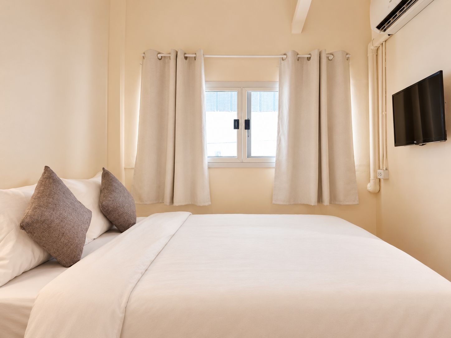 A hotel room with a bed, curtains, a television, and an air conditioning unit.