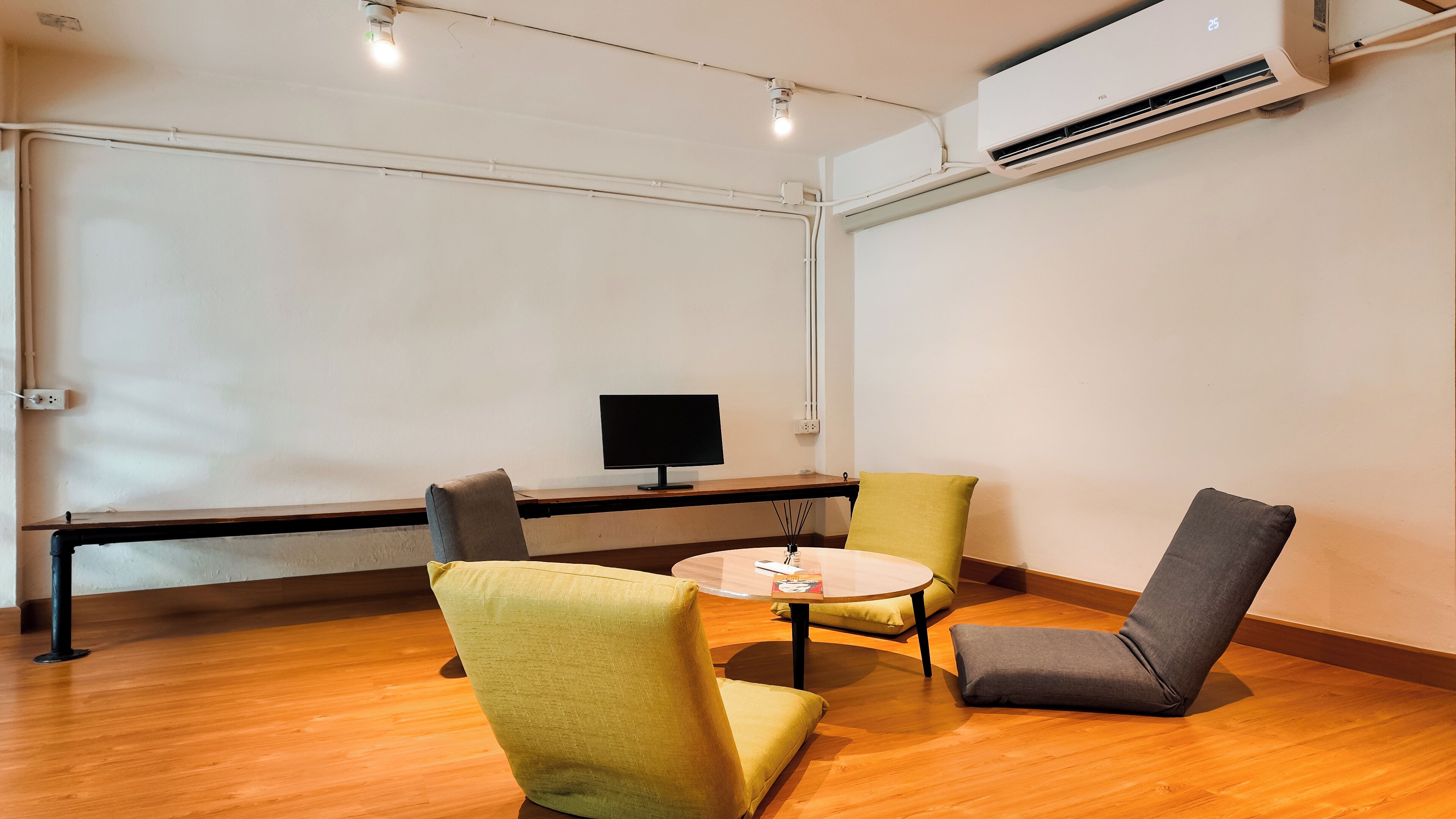 A conference room with a round table, two chairs, a flat-screen TV, and an air conditioning unit on the wall.