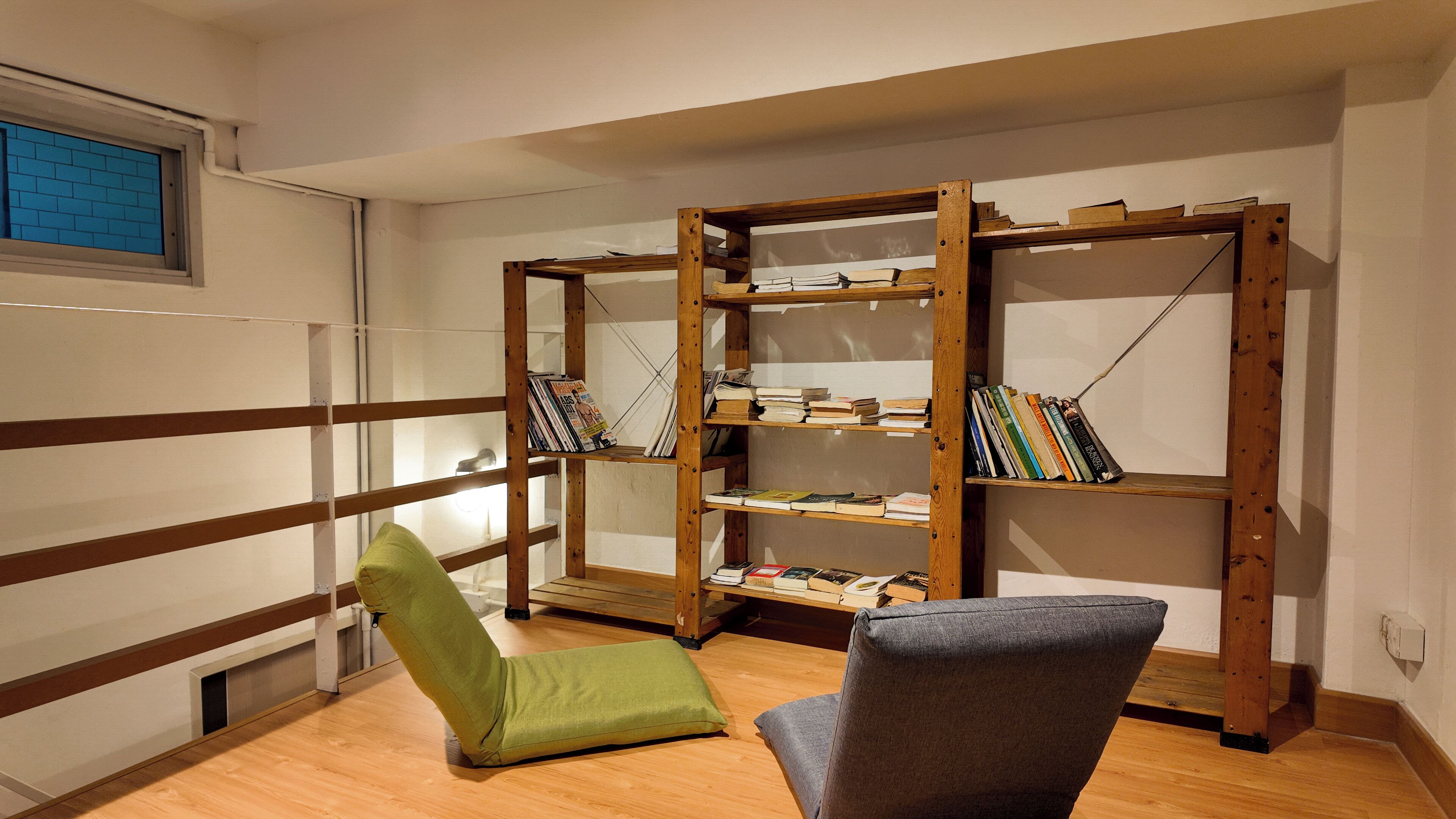 A reading nook with a wooden bookshelf, a green chair, and a grey armchair.