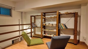 Un rincón de lectura con una estantería de madera, un sillón verde y un sillón gris.