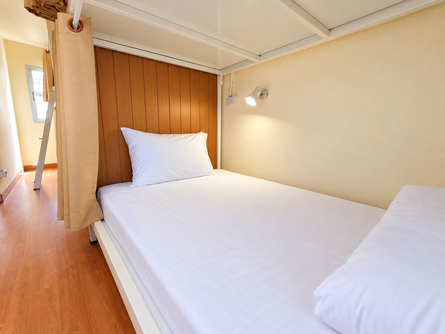 A single bed with a wooden headboard, white bedding, and a wall-mounted light fixture.