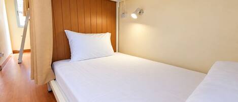 A single bed with a wooden headboard, white bedding, and a wall-mounted light fixture.