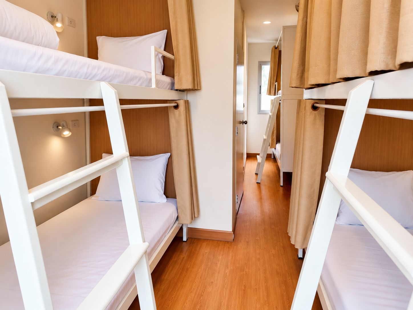 A corridor with bunk beds, wooden flooring, and beige curtains.