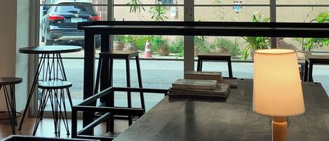 A room with a large window, a wooden table with a lamp, and a view of the street outside.