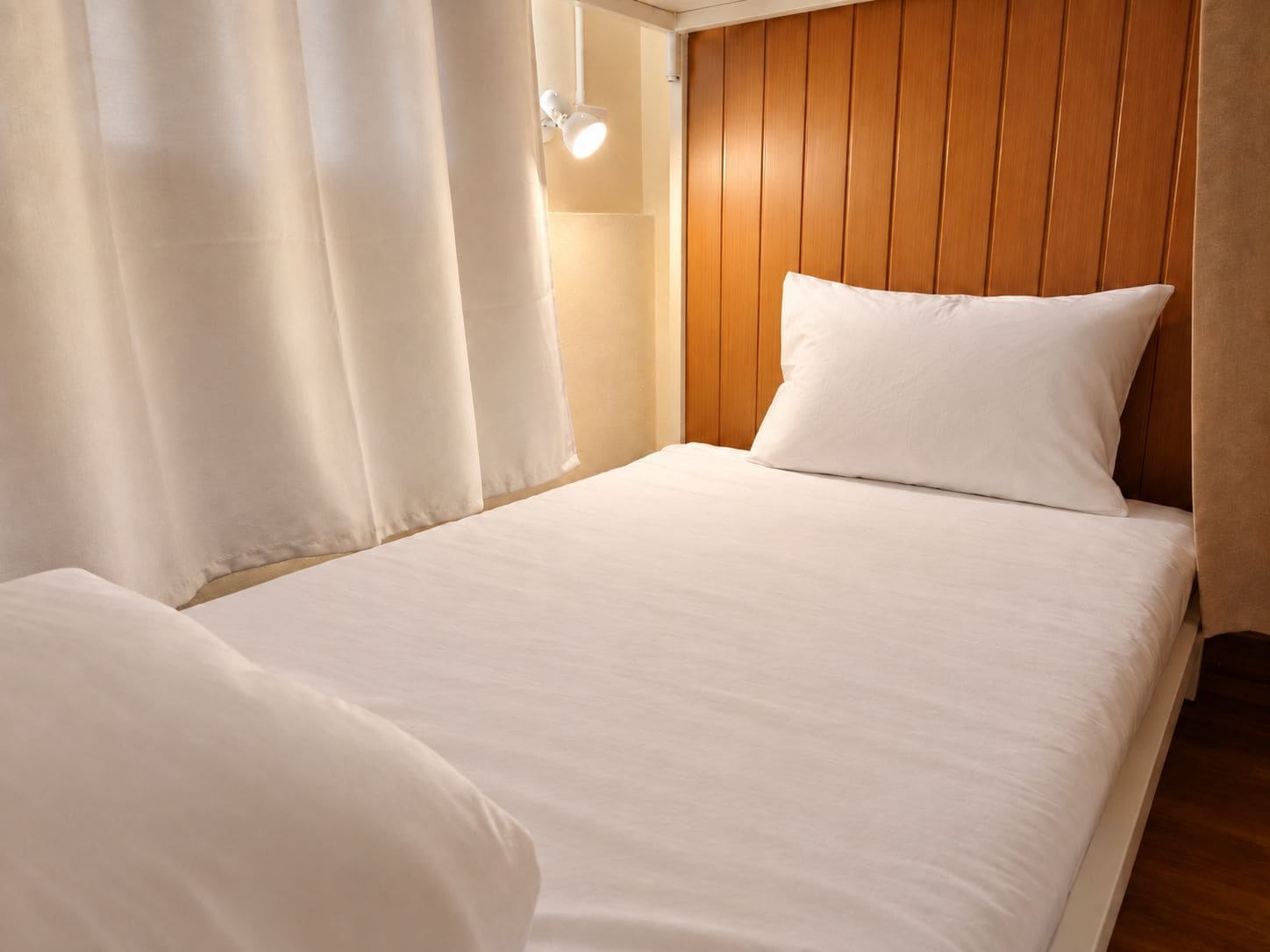 A single bed with white bedding in a room with wooden paneling on the wall.