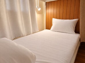 Una cama individual con ropa blanca en una habitación con paneles de madera.