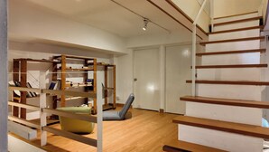 Una habitación con una escalera de madera, una estantería y un banco acolchado.