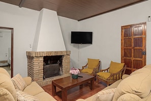A living room with a stone fireplace, a flat-screen TV mounted on the wall, and a wooden door. - Country House 'Rural La Armona' with Private Garden, Wi-Fi and Air Conditioning (La Carlota)