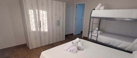 A room with a bunk bed, a wardrobe, and a door leading to another room.