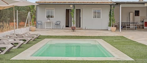 A residential property with a swimming pool, outdoor seating, and a covered patio area.