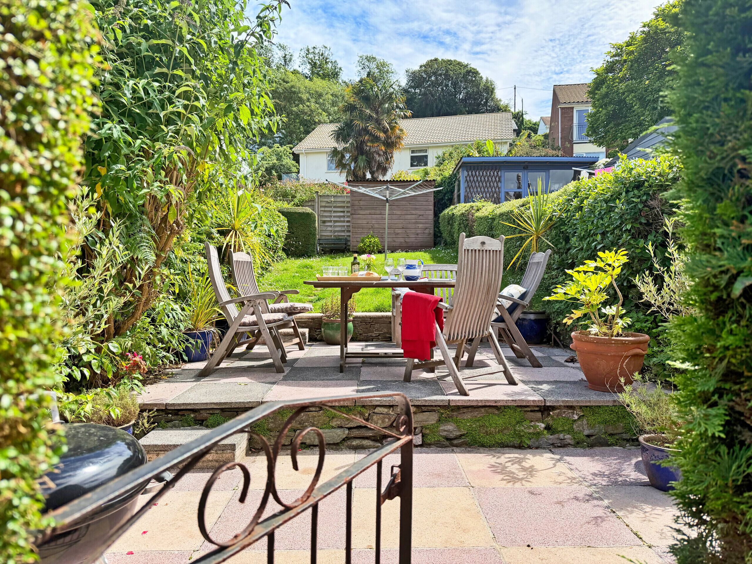 A patio area with a table and chairs, surrounded by potted plants and a view of a house.