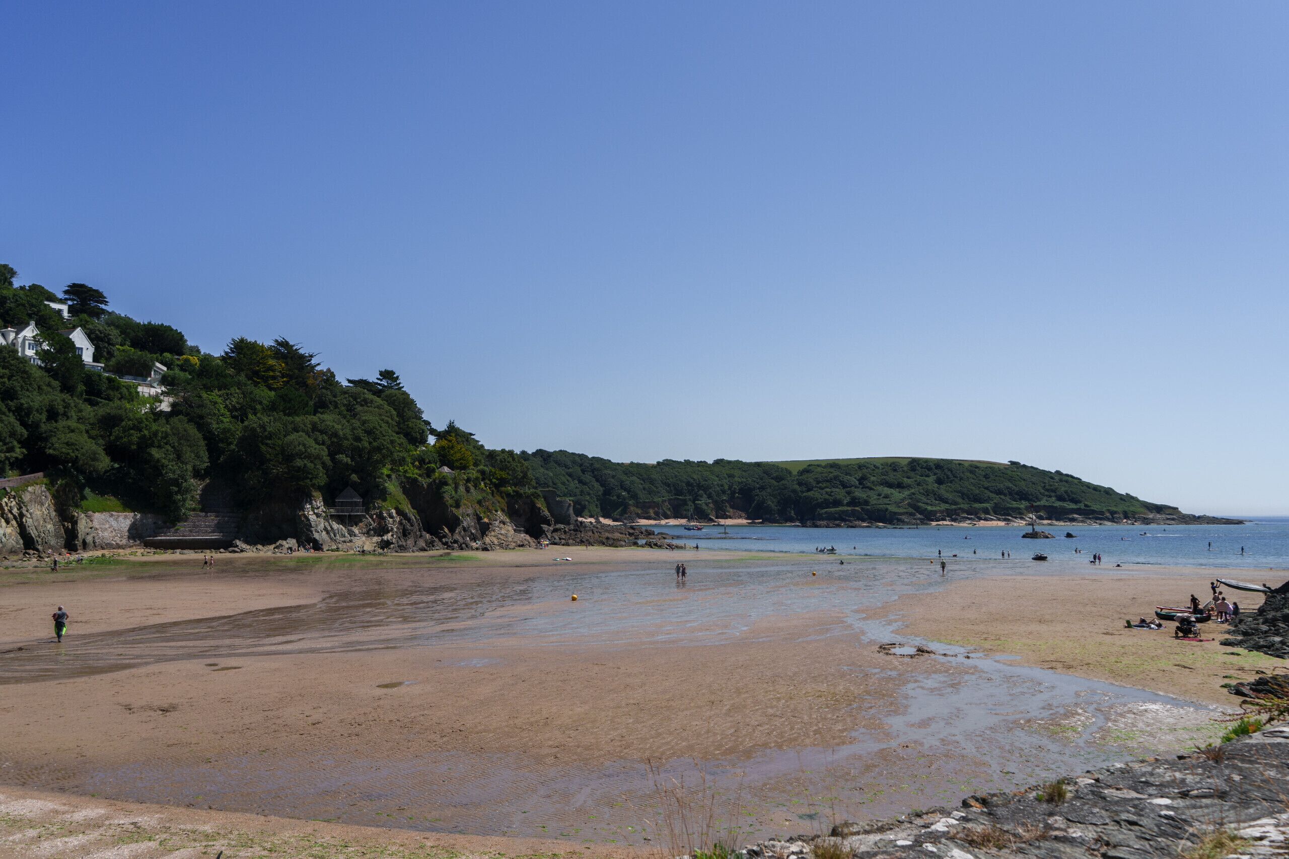 A beach with a sandy shore, rocky outcrops, and a forested hillside.