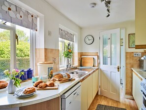 A kitchen with a large window, a clock, and a door leading to another room. - Finest Retreats | Garston (Salcombe)