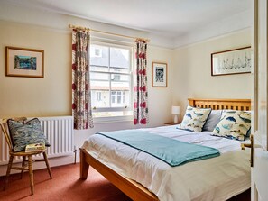 A bedroom with a bed, a chair, a window with curtains, and two framed pictures on the wall. - Finest Retreats | Garston (Salcombe)