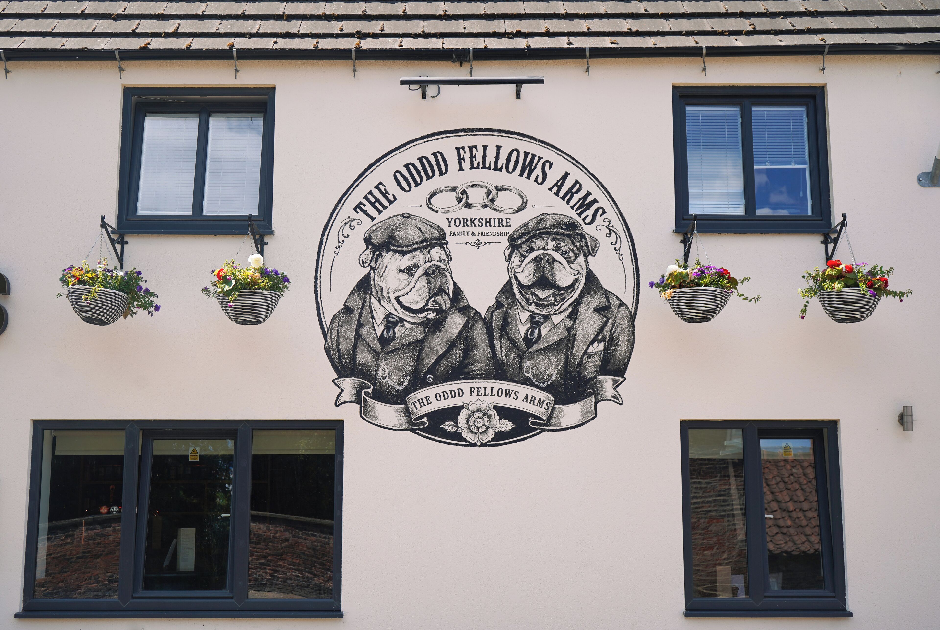 Un edificio con un emblema circular que muestra dos perros y el texto 'The Odd Fellows Arms Yorkshire Family & Friendship'.