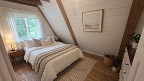Ein Schlafzimmer mit Bett, Nachttisch, Lampe, Fenster und einem gerahmten Bild an der Wand.