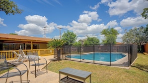 A backyard with a swimming pool, a covered patio with chairs, and a wooden deck. - The Airman House Pool-hot Tub-fun by Lackland AFB (San Antonio)
