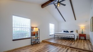 A bedroom with a sloped ceiling, wooden flooring, a bed with white bedding, two bedside tables with lamps, and a window with blinds. - The Airman House Pool-hot Tub-fun by Lackland AFB (San Antonio)