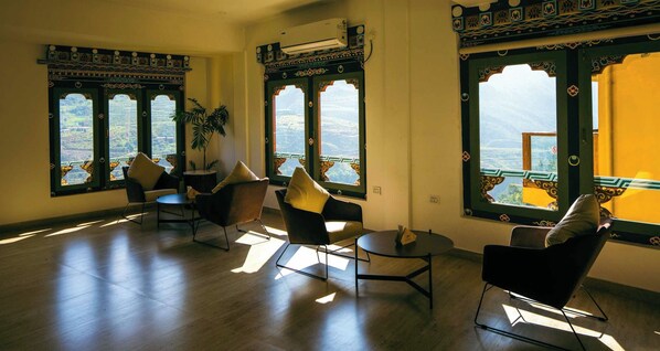 Amplia habitación con un gran ventanal que ofrece vistas a un paisaje montañoso. Hay varias sillas y una mesita, y la habitación presenta un diseño moderno con marcos de ventana estampados.