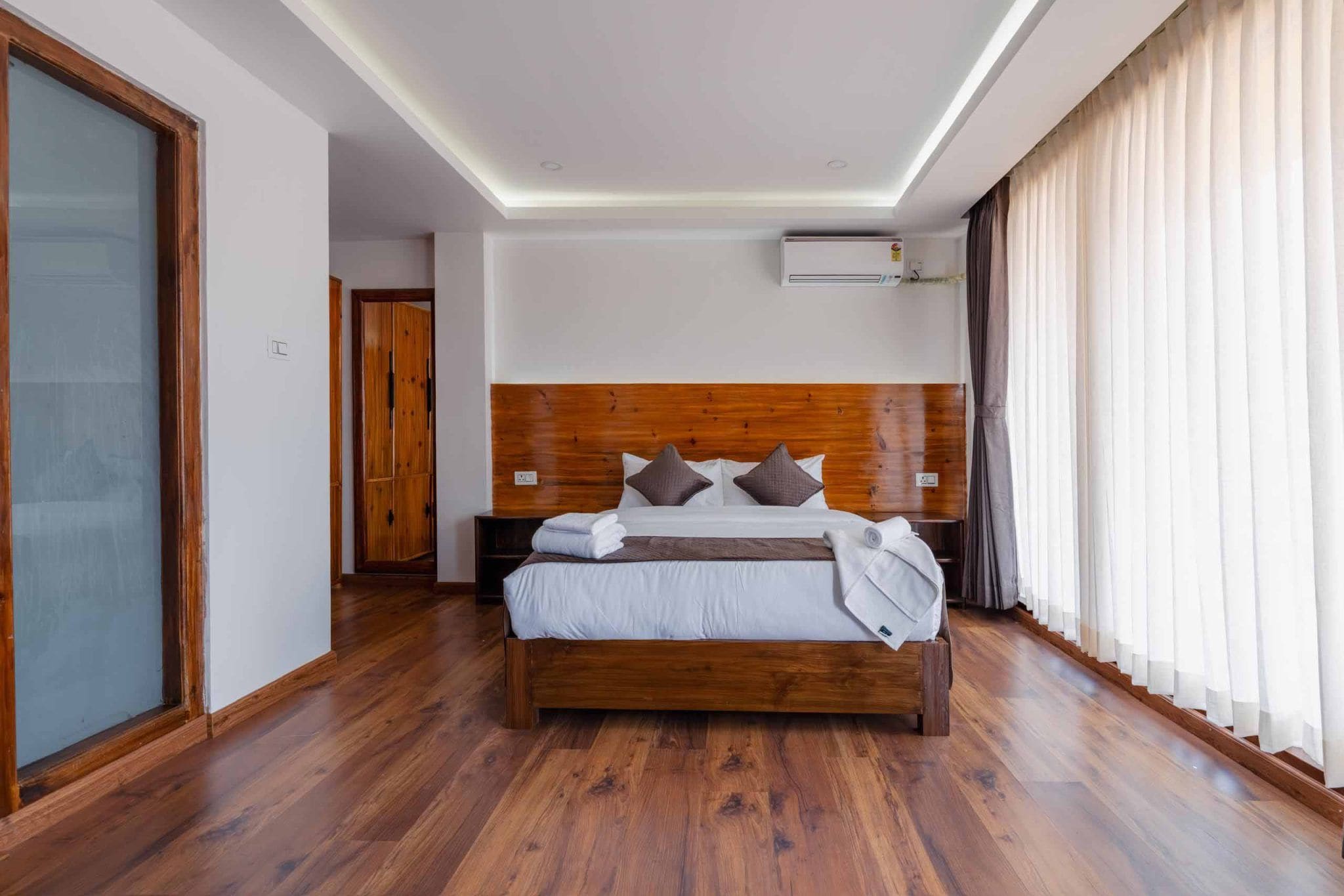 Un dormitorio moderno con una cama de madera, una mesita de noche y un amplio ventanal con cortinas.
