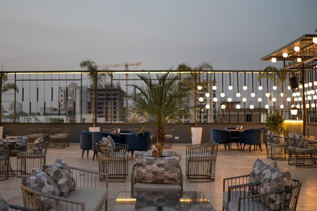Un área de estar al aire libre con mesas y sillas, una palmera y luces colgantes.