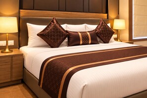 Quarto de hotel com uma cama, duas luminárias de cabeceira, mesa de apoio e uma janela com persianas.