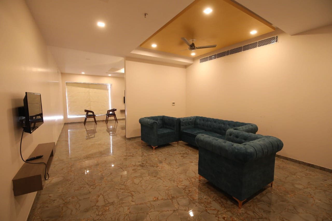 A spacious room with a sectional sofa, a flat-screen TV mounted on the wall, and a ceiling fan.