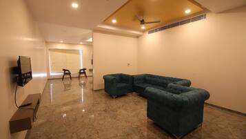 A spacious room with a sectional sofa, a flat-screen TV mounted on the wall, and a ceiling fan.