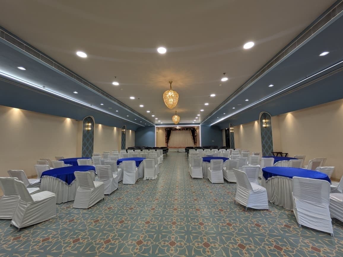 Uma sala de conferências com fileiras de cadeiras e mesas, um tapete estampado e um lustre.