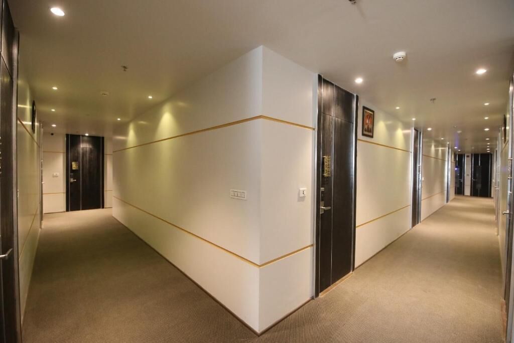Um corredor com piso coberto por carpete, paredes brancas com detalhes dourados e portas que dão acesso a quartos.