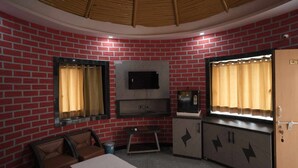 Habitació amb paret de maó, televisió penjada sobre un moble, un llit i una porta amb un número.
