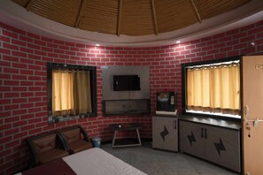 A room with a brick wall, a television mounted above a cabinet, a bed, and a door with a number. - Surya Resort, Peaceful Stay with Modern Comforts (Chittorgarh)
